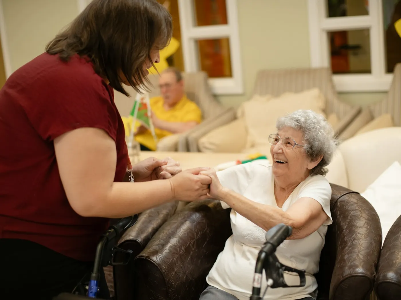A carer holding an older resident's hands in a care-home lounge