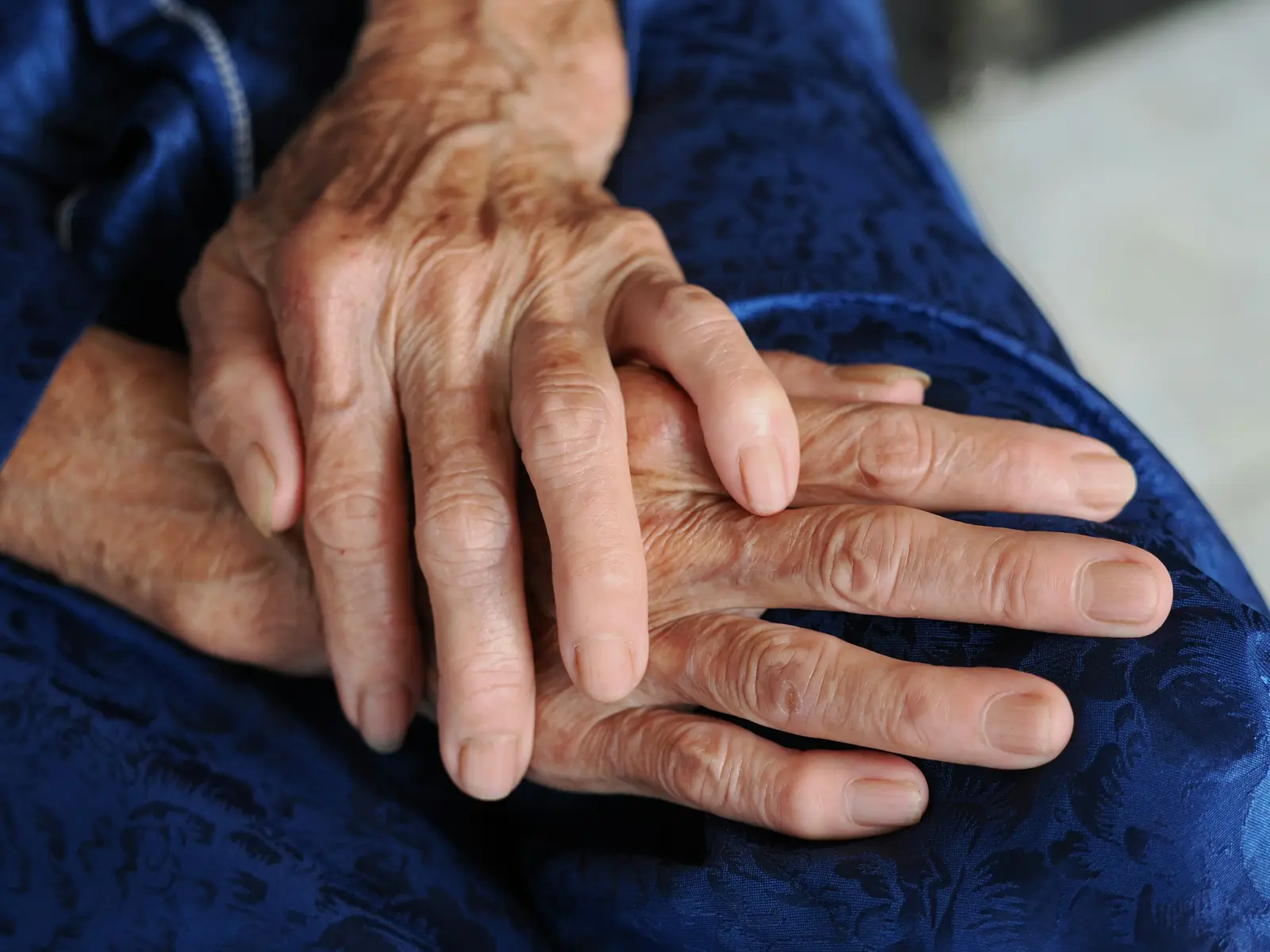An older person's hands resting together on blue cloth